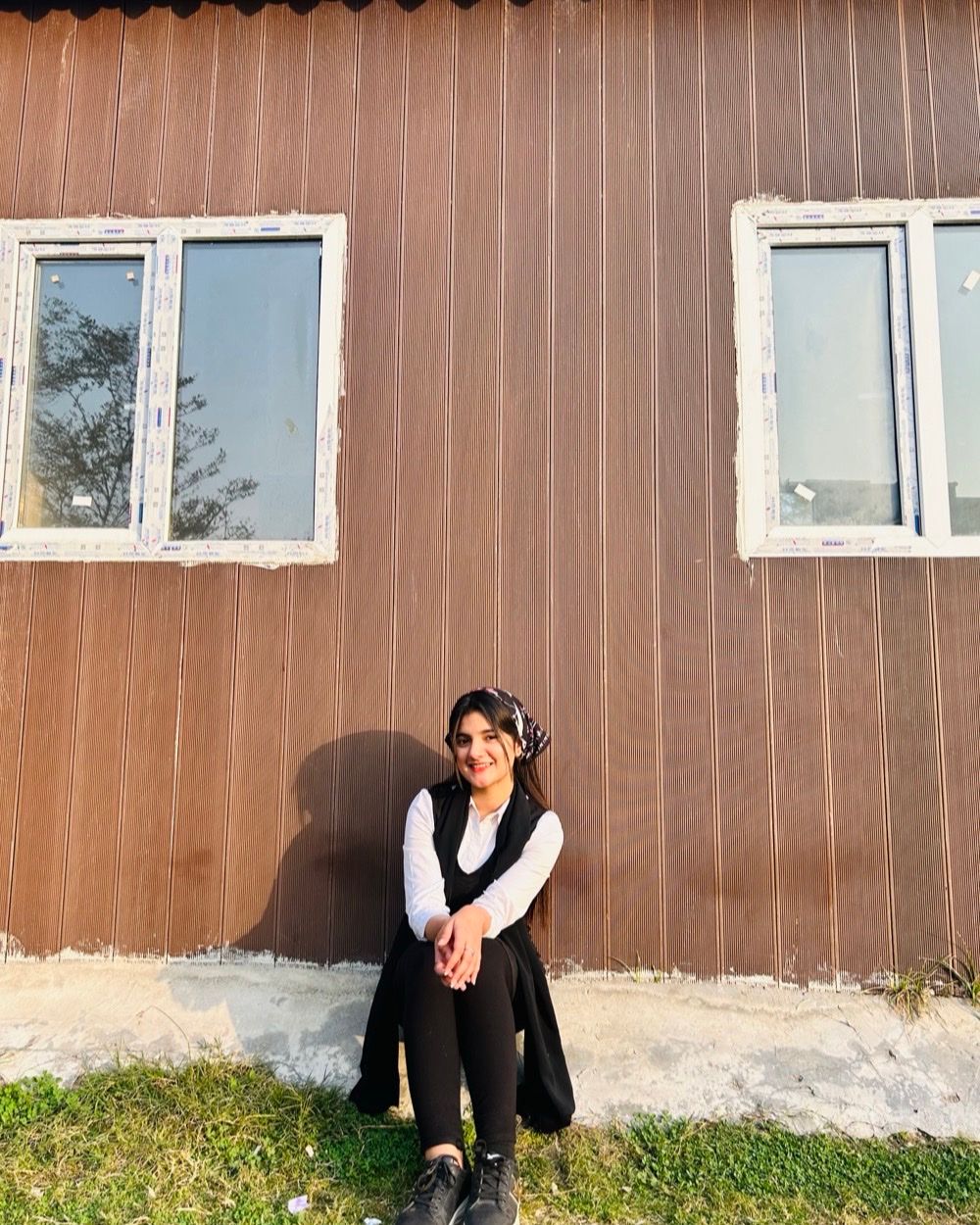 Eman Ashfaq sitting outdoors against a corrugated wall